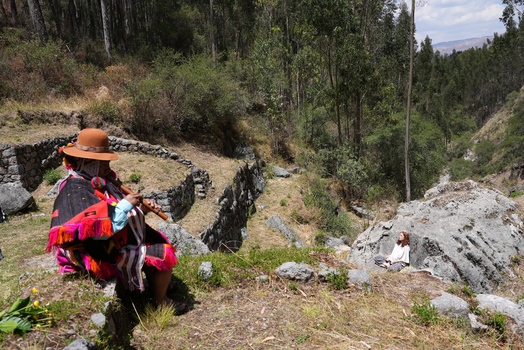 A Quechua musician playing a flute for a traveler meditating among Inca terraces in the Peruvian Andes